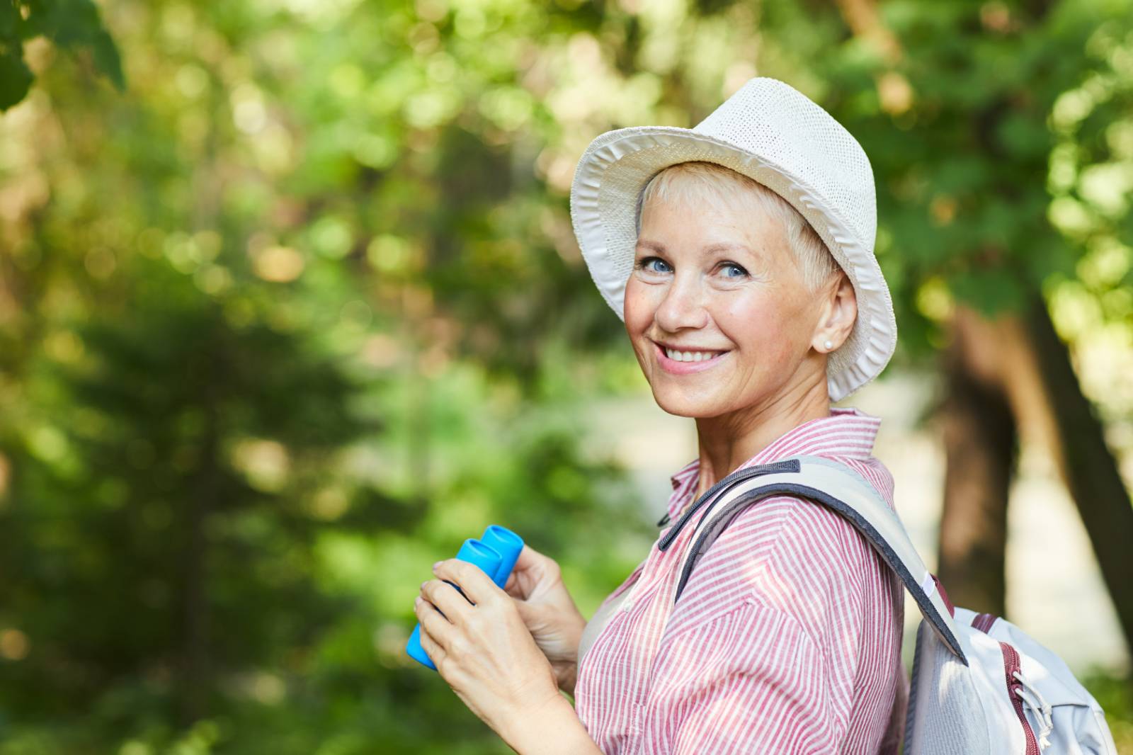 Smiling woman in a hat holding binoculars outdoors.