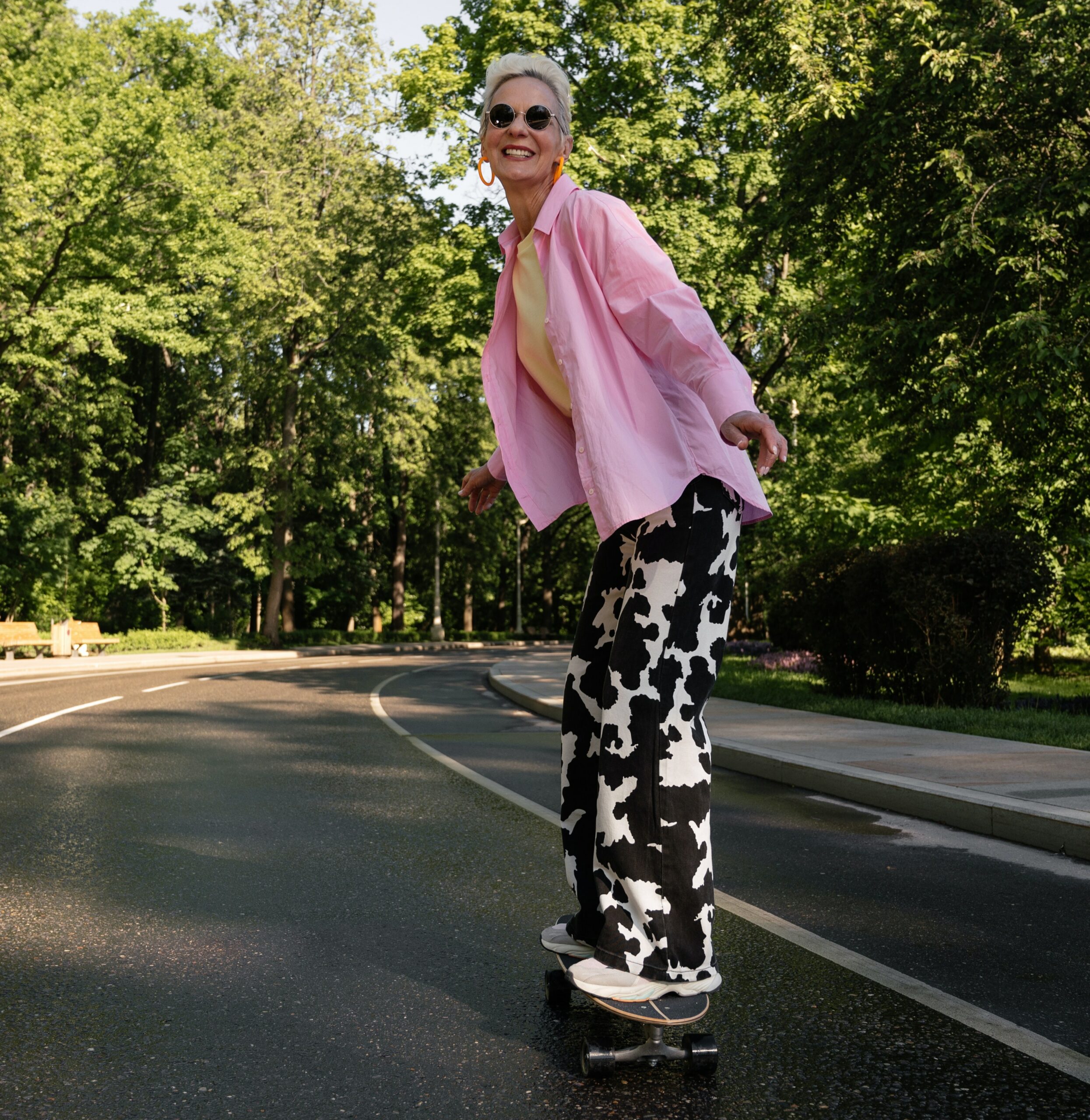 Person skateboarding on a sunny road wearing cow-print pants and a pink shirt.
